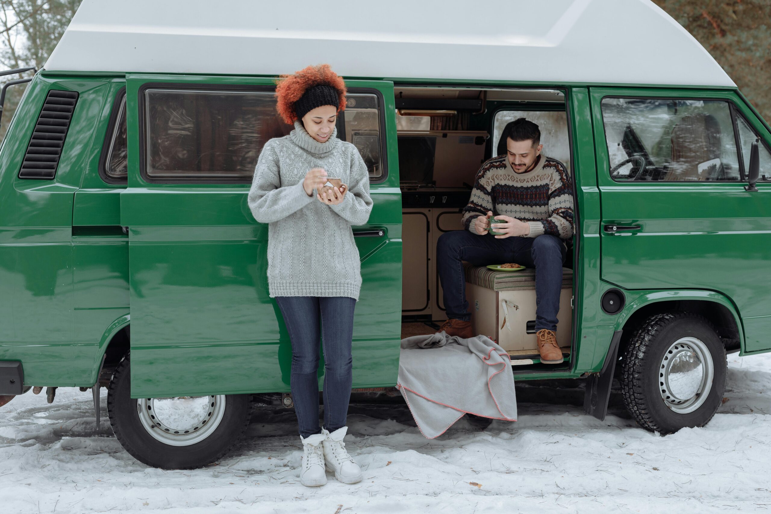 Couple enjoying hot drinks beside a camper van in the snow